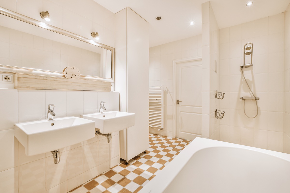 Sinks with mirrors and clean bathtub located near shower box with glass door in modern bathroom with white tiled walls