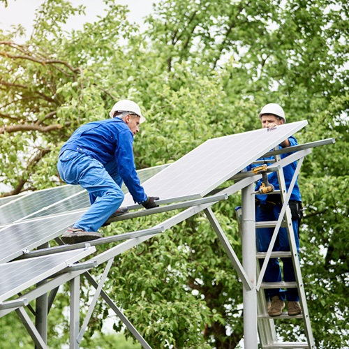 Installing of stand-alone solar photo voltaic panel system. Two workers assembling solar modules on metal platform on green tree background. Alternative energy and professional construction concept.
