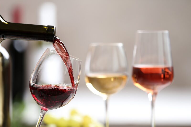Pouring red wine from bottle into glass on blurred background. Space for text