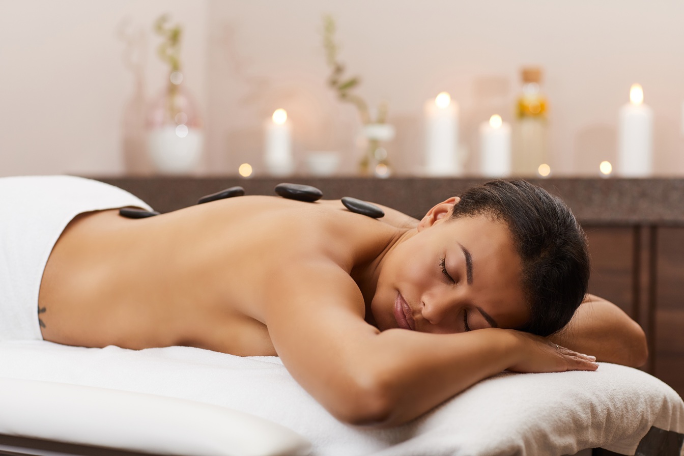 Side view portrait of beautiful mixed-race woman lying on massage table during stone therapy in SPA, copy space