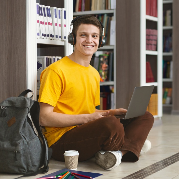 Creative caucasian guy sitting on the floor at library, working on new project and using laptop