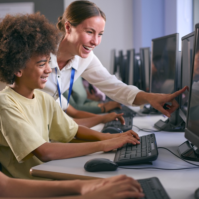 Group Of Secondary Or High School Students At Computers In IT Class With Female Teacher